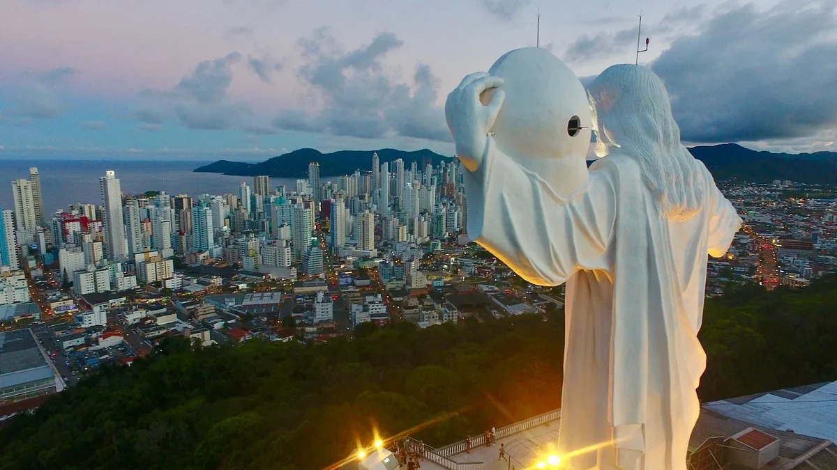 Monumento Cristo Luz iluminado ao anoitecer, com o skyline de Balneário Camboriú ao fundo.