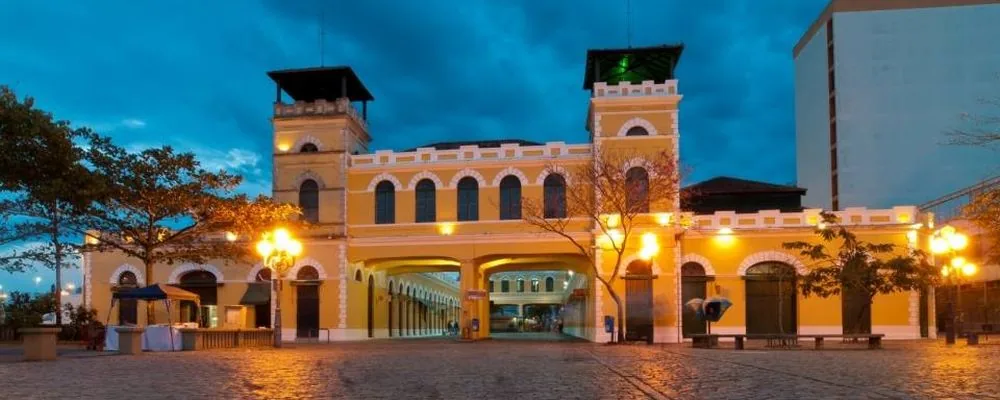 Fachada amarela iluminada do Mercado Público de Florianópolis ao anoitecer.