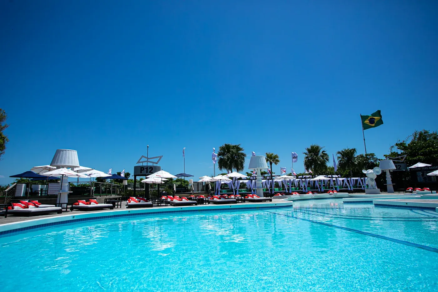 Área da piscina do beach club P12 em Jurerê Internacional, Florianópolis, com espreguiçadeiras e dia ensolarado.