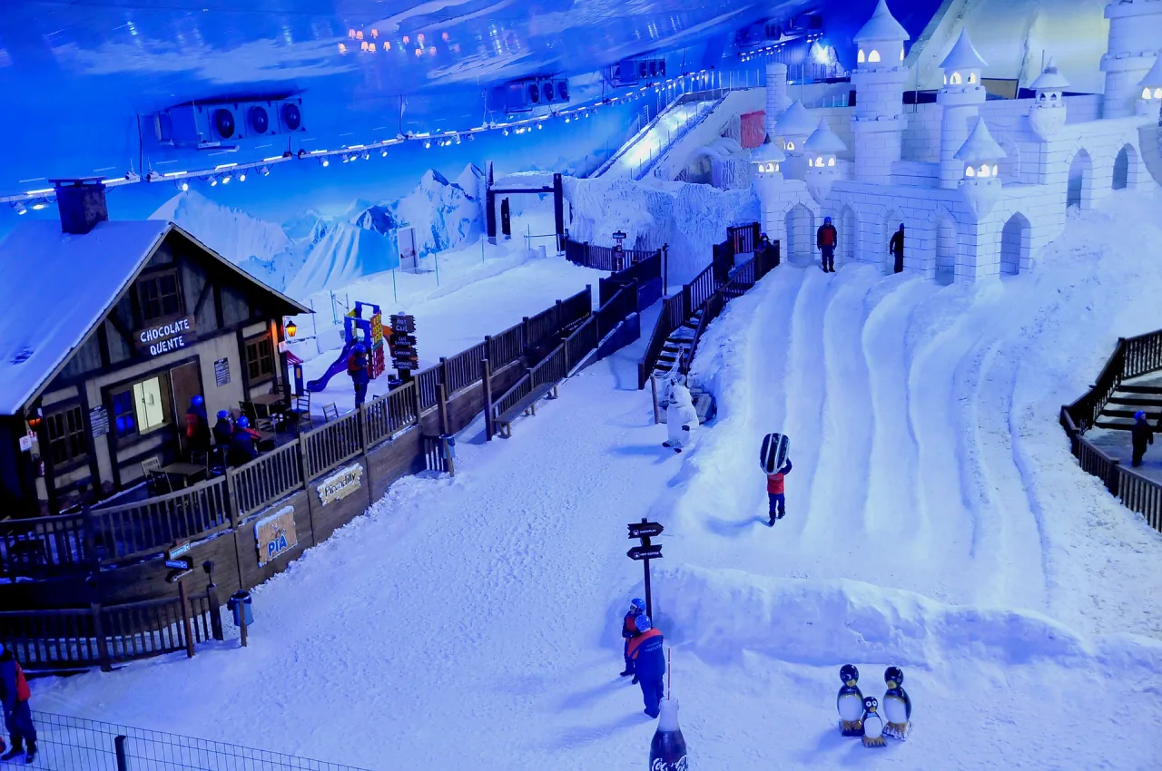 Interior do Snowland em Gramado, com neve de verdade, castelo de gelo e pessoas brincando na pista.